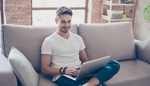 Young attractive smiling guy is browsing at his laptop, sitting